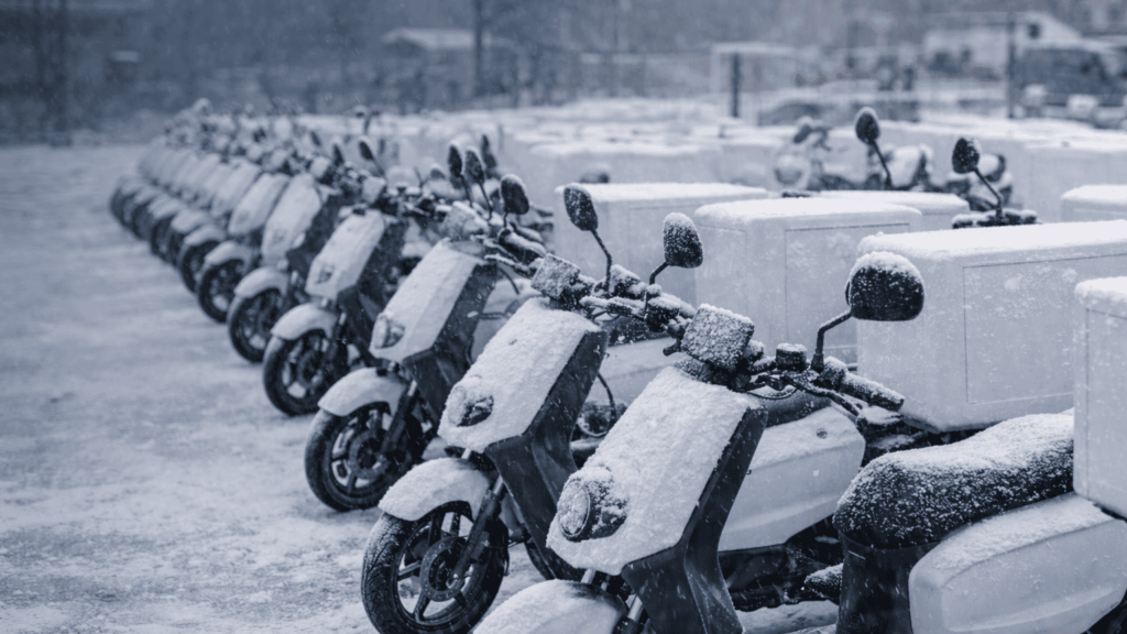 Flota de motos eléctricas de reparto estacionadas en invierno, con nieve, mostrando cómo el frío afecta a la autonomía.