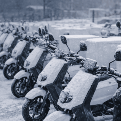 Flota de motos eléctricas de reparto estacionadas en invierno, con nieve, mostrando cómo el frío afecta a la autonomía.